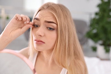 Young woman with eyelash loss problem looking in mirror indoors