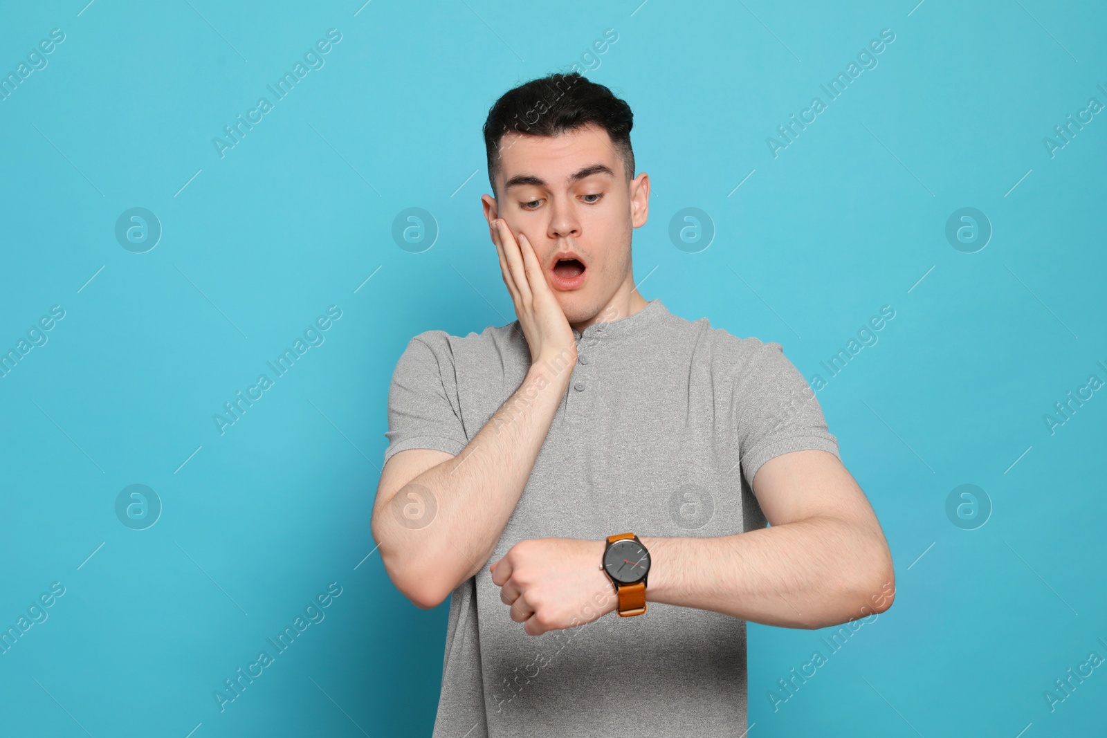 Photo of Emotional young man checking time on light blue background. Being late concept