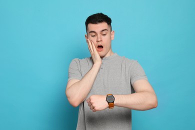 Photo of Emotional young man checking time on light blue background. Being late concept