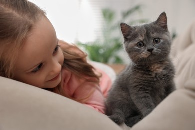 Cute little girl with kitten on sofa at home, closeup. Childhood pet