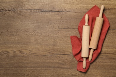 Photo of Rolling pins and napkin on wooden table, flat lay with space for text. Cooking utensils