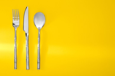 Photo of Spoon, fork and knife on yellow background, flat lay. Space for text