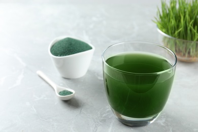 Photo of Glass of spirulina drink and powder on table, space for text