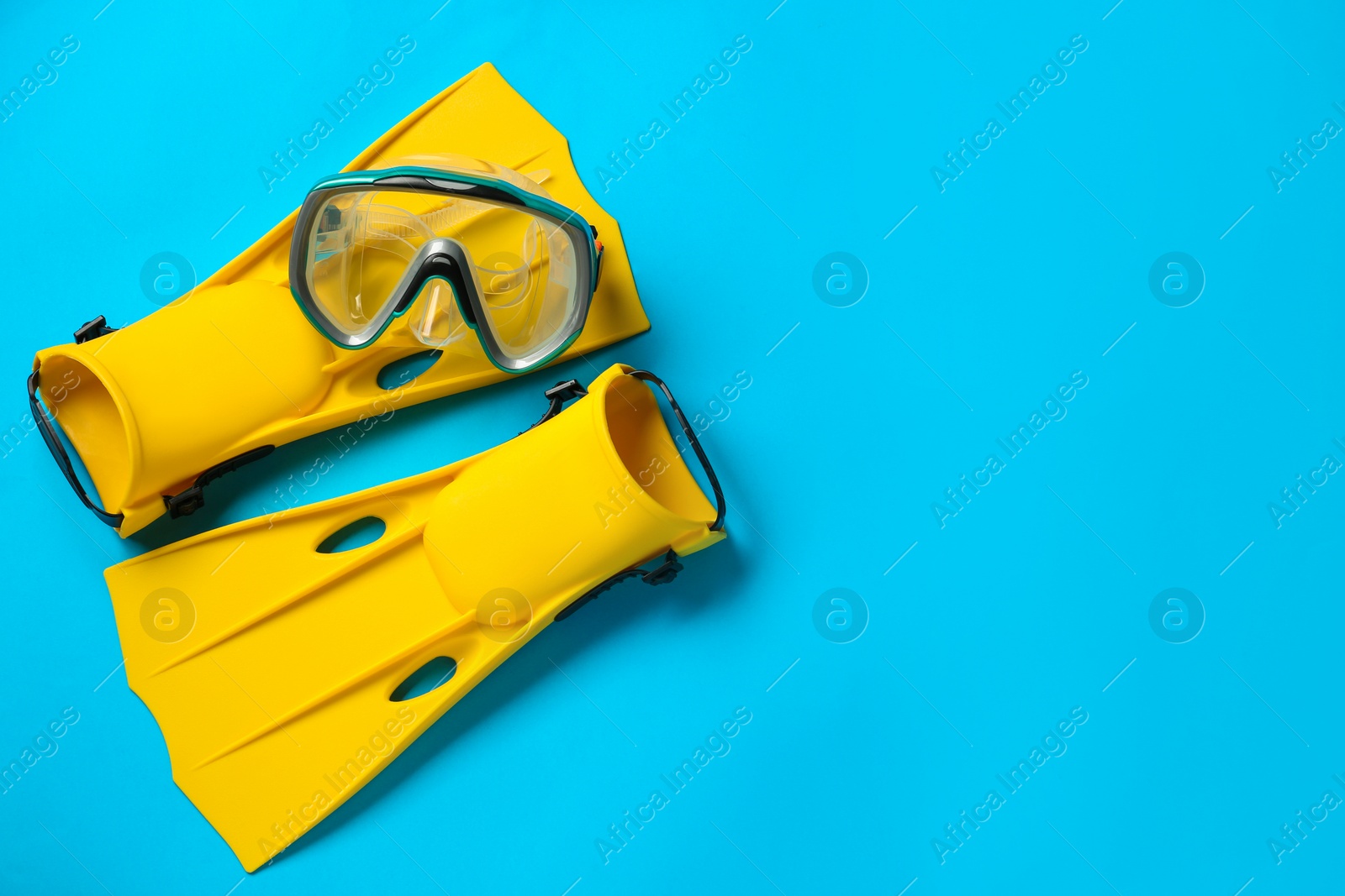 Photo of Pair of yellow flippers and mask on light blue background, flat lay. Space for text