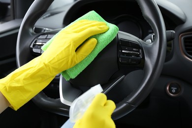 Photo of Woman cleaning steering wheel with rag in car, closeup