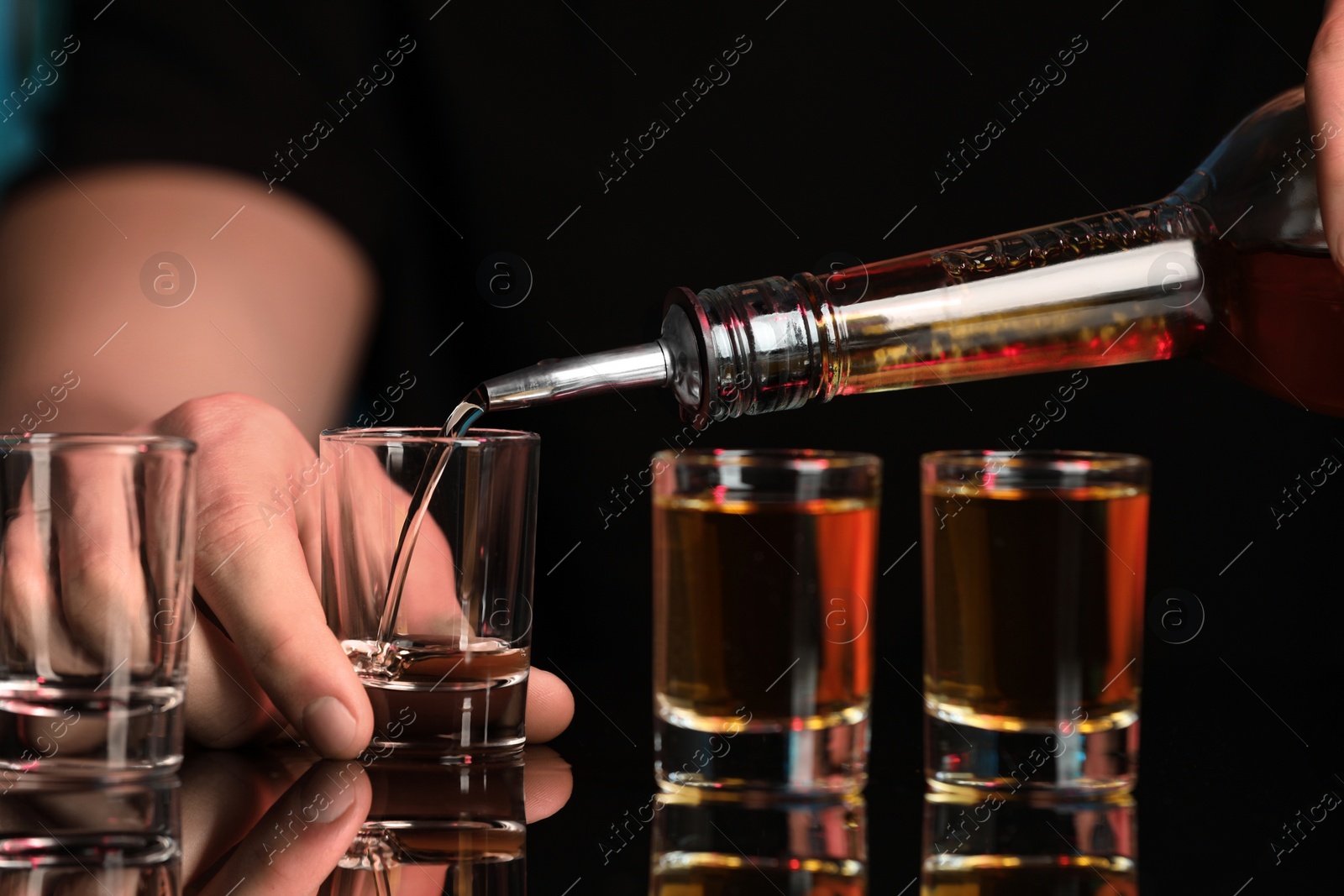 Photo of Bartender pouring alcohol drink into shot glass at mirror bar counter, closeup