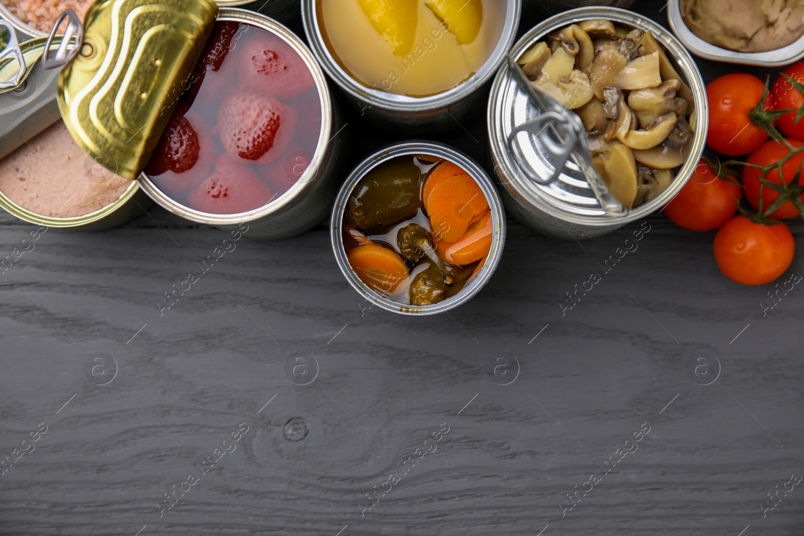 Photo of Open tin cans with different products on gray wooden table, flat lay. Space for text