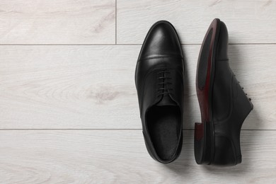 Photo of Pair of black leather men shoes on light wooden floor, top view. Space for text