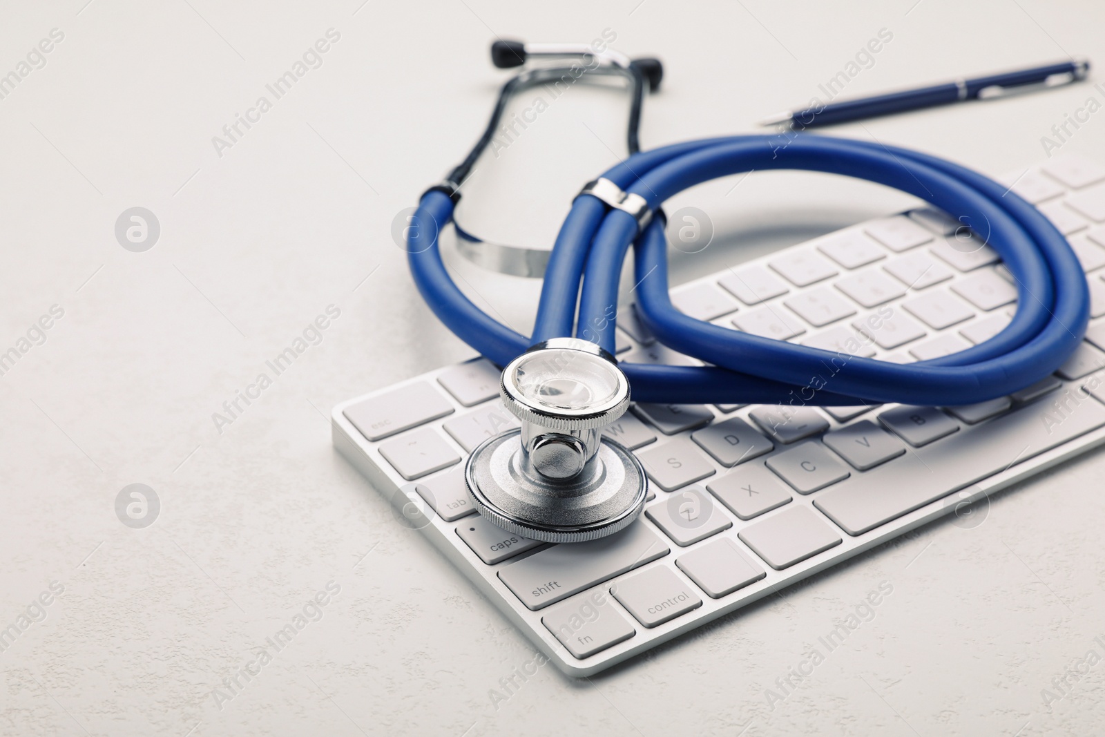 Photo of Computer keyboard with stethoscope on white table, closeup. Space for text