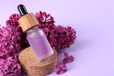 Bottle with essential oil and lilac flowers on violet background, space for text
