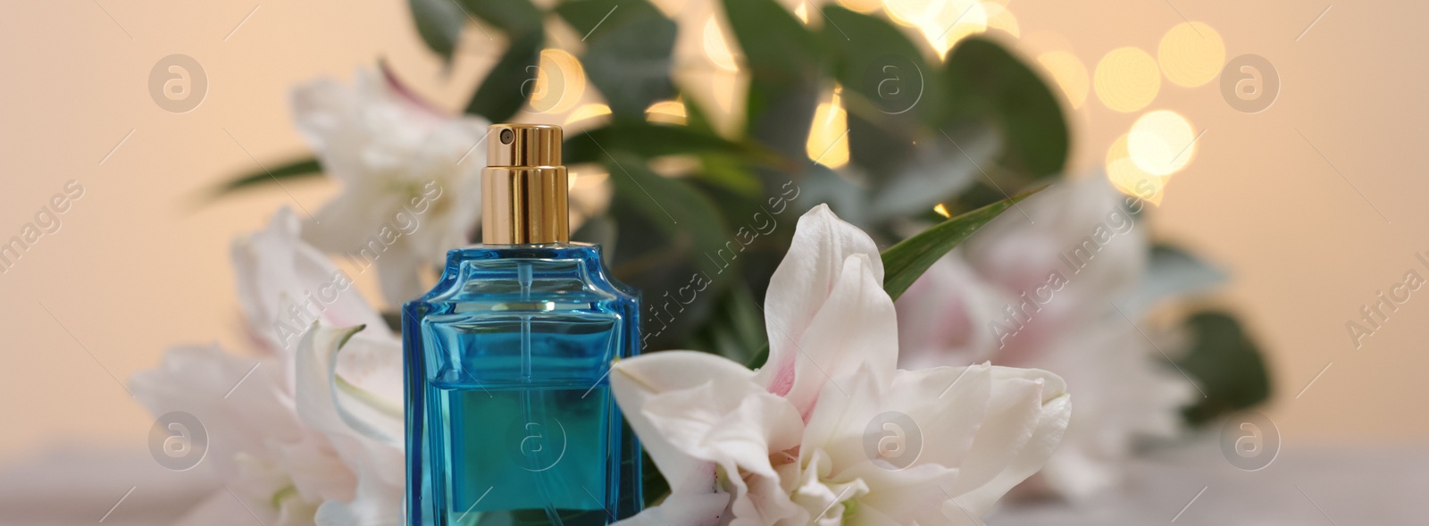 Photo of Bottle of perfume and beautiful lily flowers against beige background with blurred lights, closeup