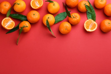Photo of Fresh ripe tangerines with green leaves on red background, flat lay. Space for text