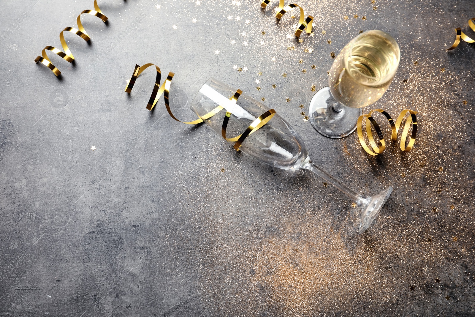 Photo of Champagne glasses and serpentine streamers on grey table, view from above. Space for text