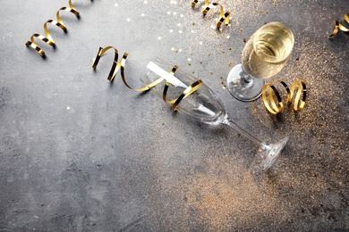 Photo of Champagne glasses and serpentine streamers on grey table, view from above. Space for text