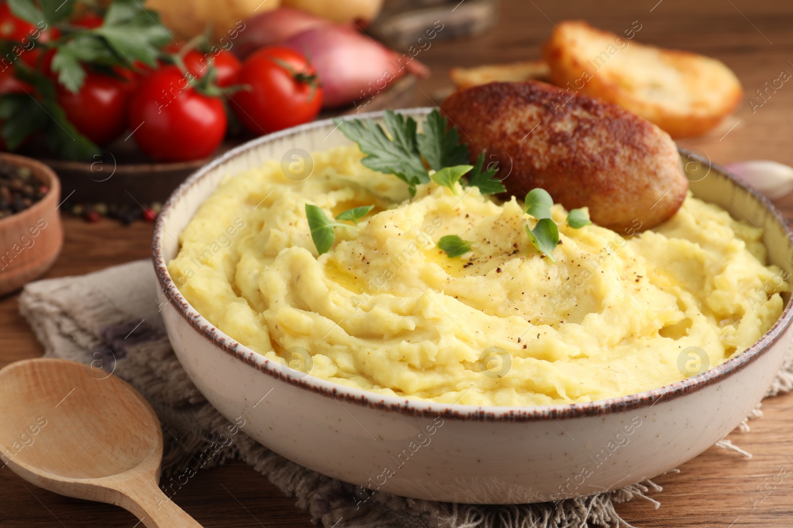 Photo of Bowl of tasty mashed potatoes with parsley, black pepper and cutlet served on wooden table, closeup