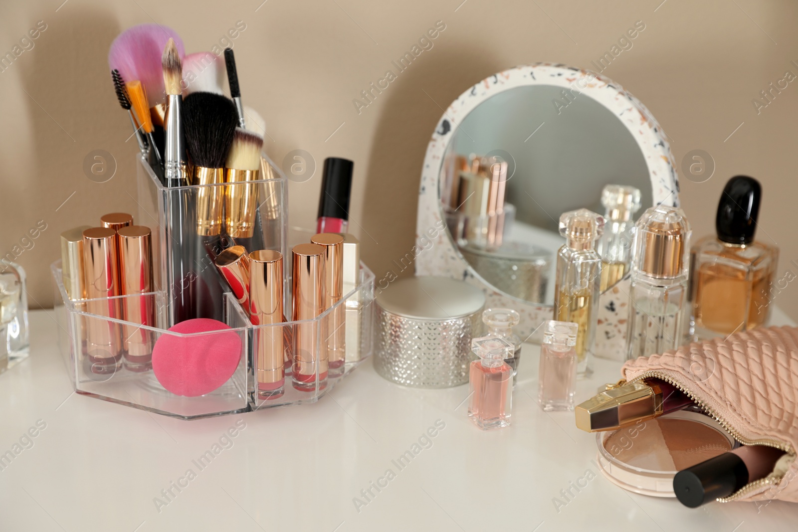 Photo of Luxury makeup products and accessories on dressing table with mirror near wall