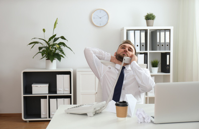 Photo of Lazy young man talking on phone at workplace