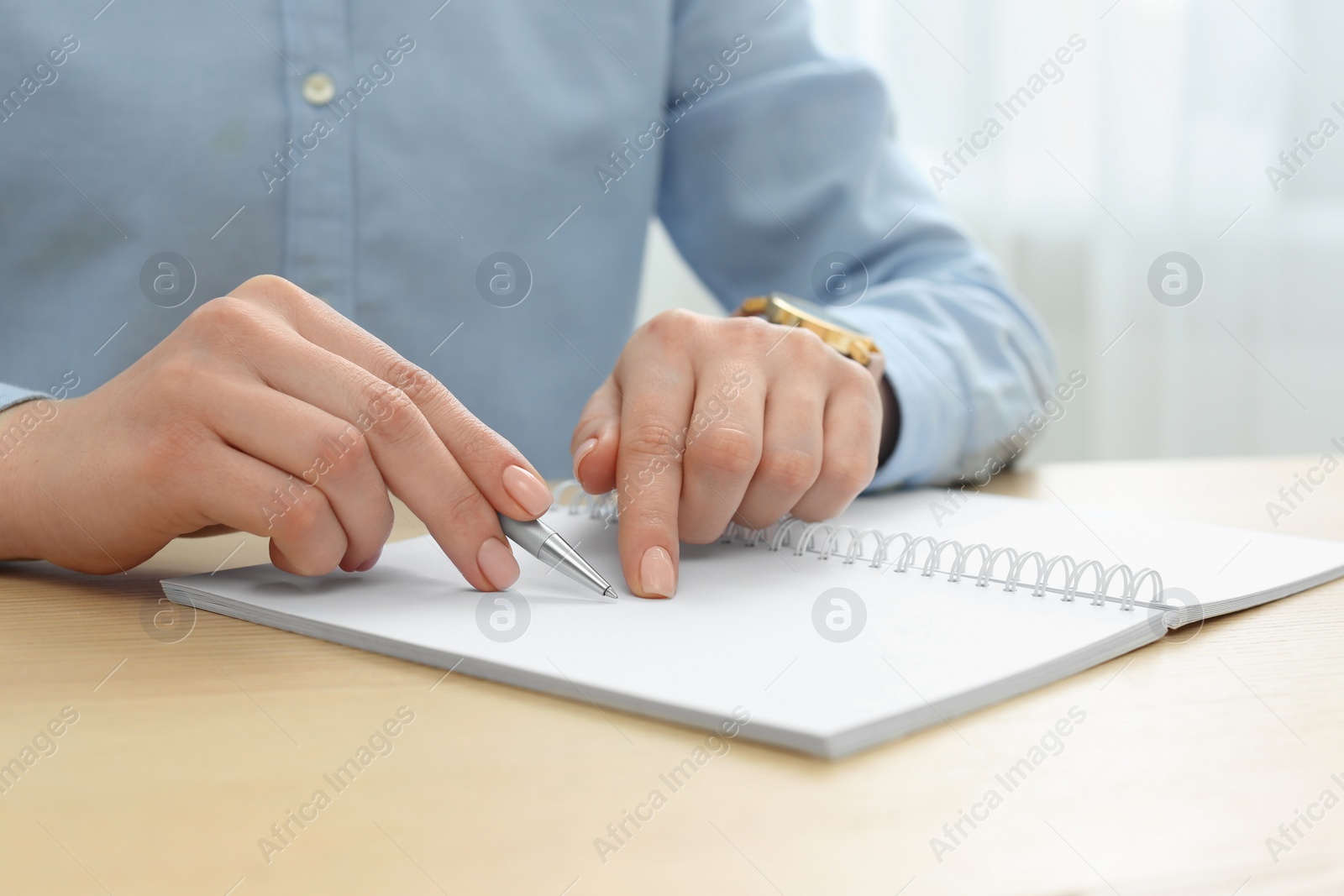 Photo of Woman writing in notebook at wooden table, closeup