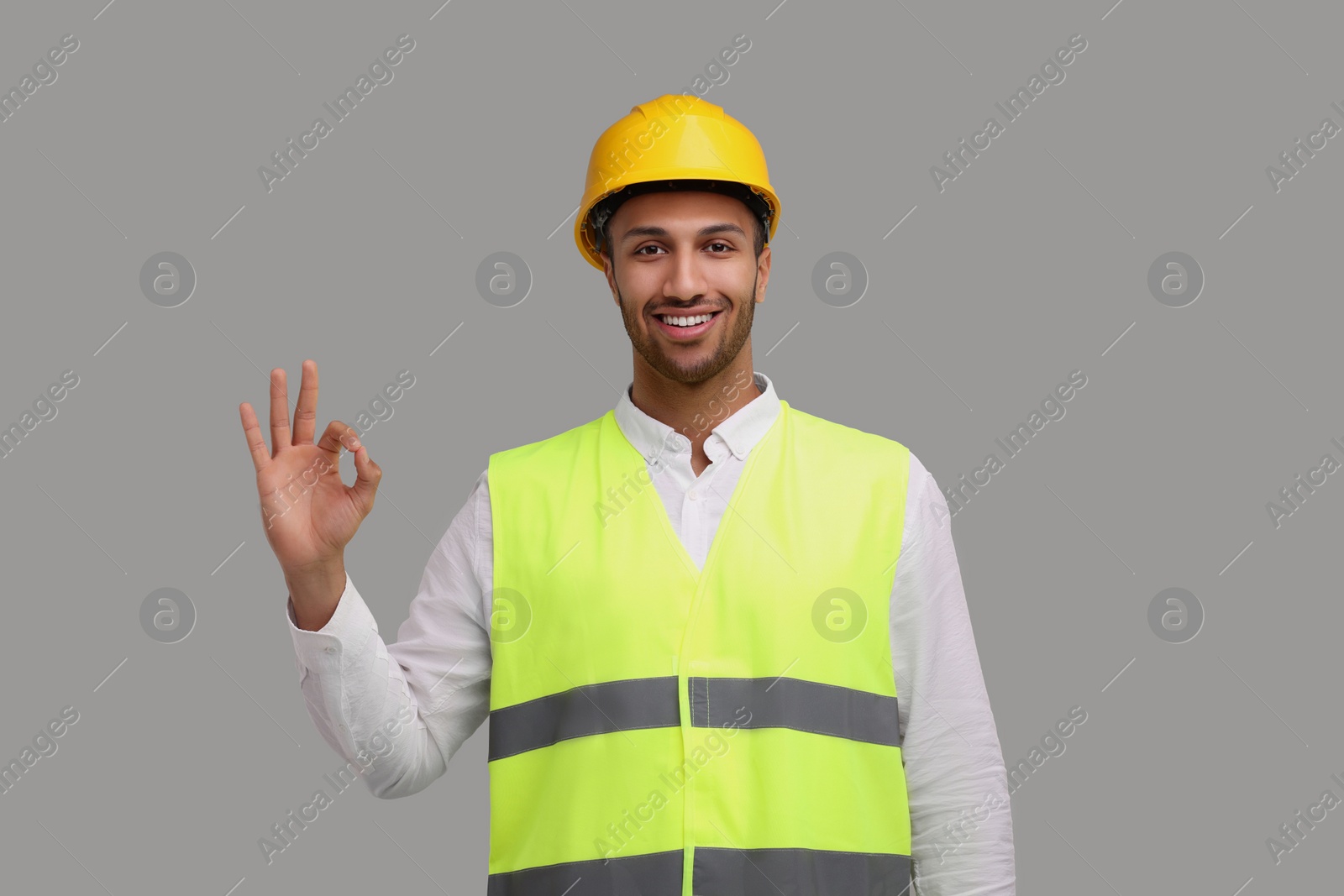 Photo of Engineer in hard hat showing ok gesture on grey background