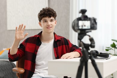Smiling teenage blogger waving hello to his subscribers while streaming at home