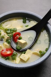 Photo of Bowl of delicious miso soup with tofu and spoon served on grey table, closeup