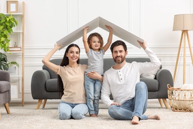 Housing concept. Happy family holding plastic roof on floor at home