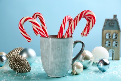 Photo of Many sweet candy canes in cup and Christmas decor on light blue wooden table