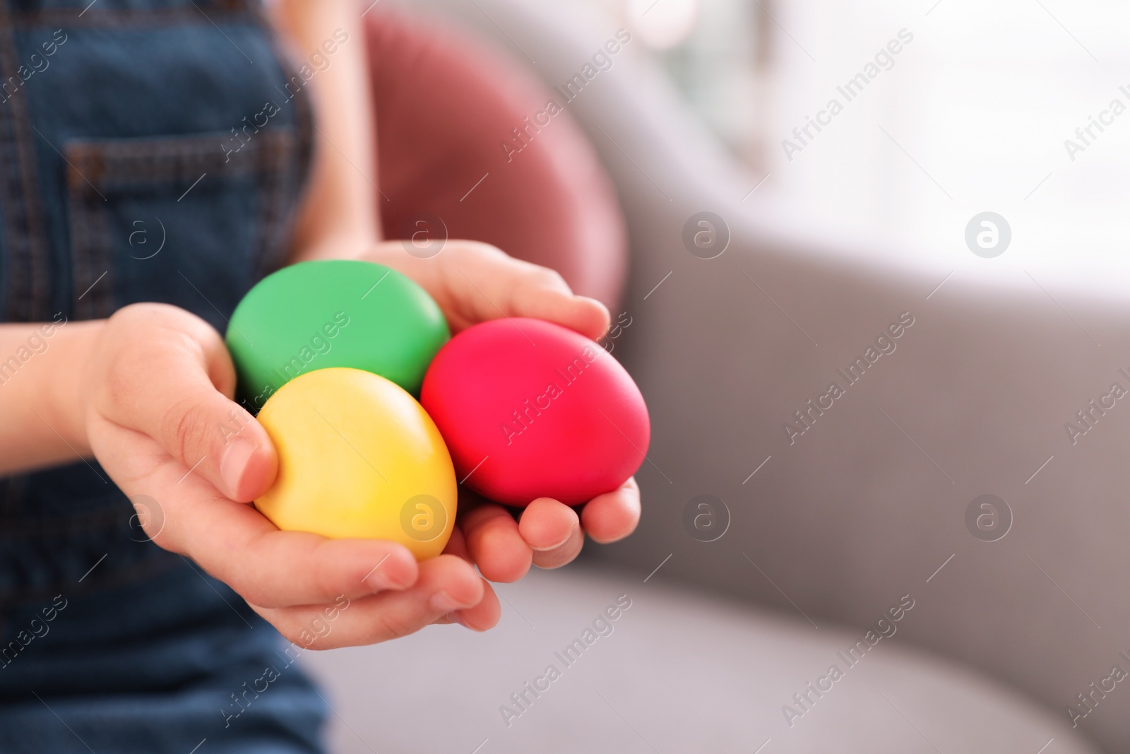 Photo of Little girl holding Easter eggs indoors, closeup. Space for text