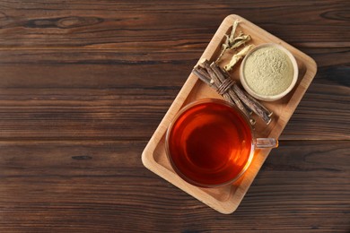 Photo of Aromatic licorice tea in cup, dried sticks of licorice root and powder on wooden table, top view. Space for text