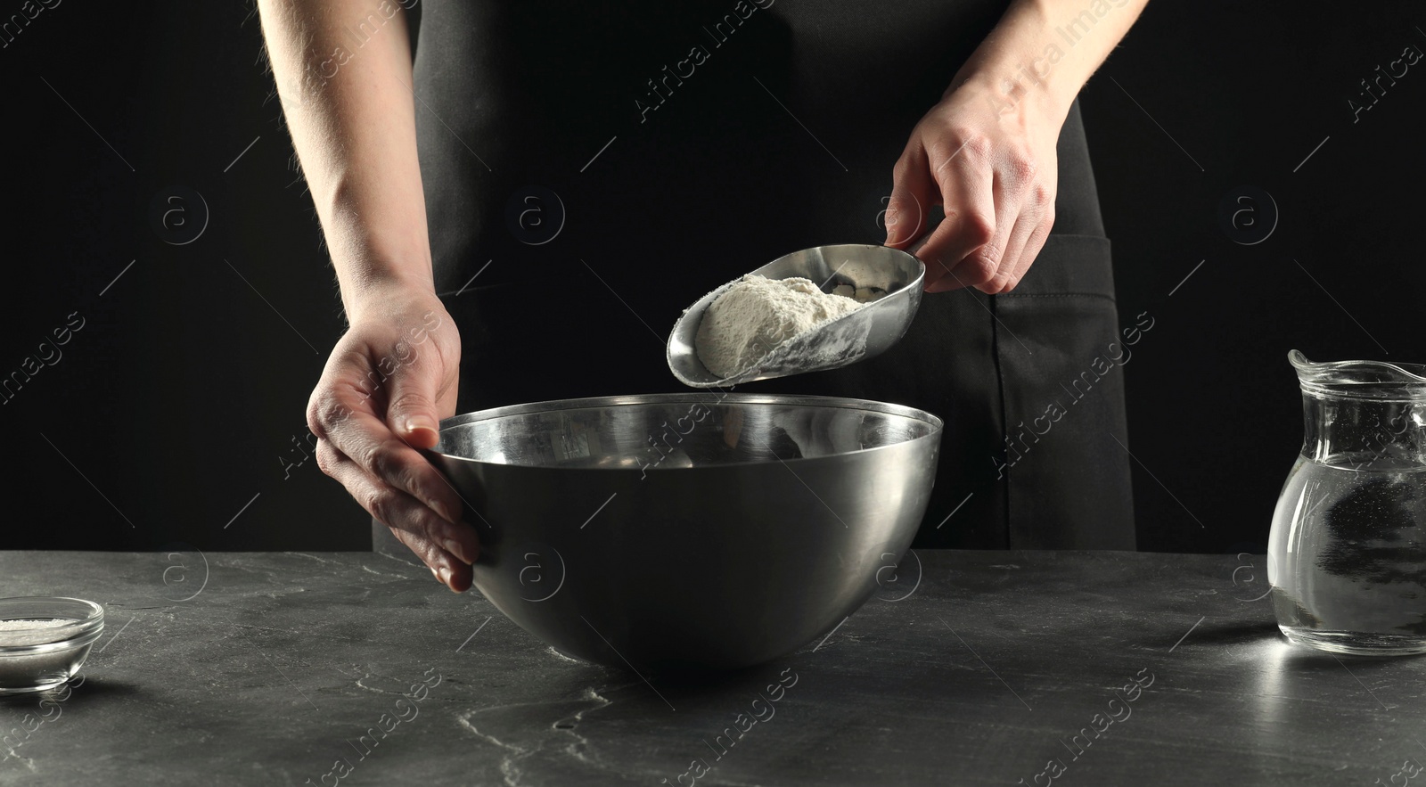 Photo of Making bread. Woman putting flour into bowl at grey textured table, closeup