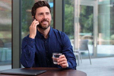 Handsome man talking on phone at table indoors