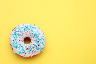 Photo of Glazed donut decorated with sprinkles on yellow background, top view. Space for text. Tasty confectionery