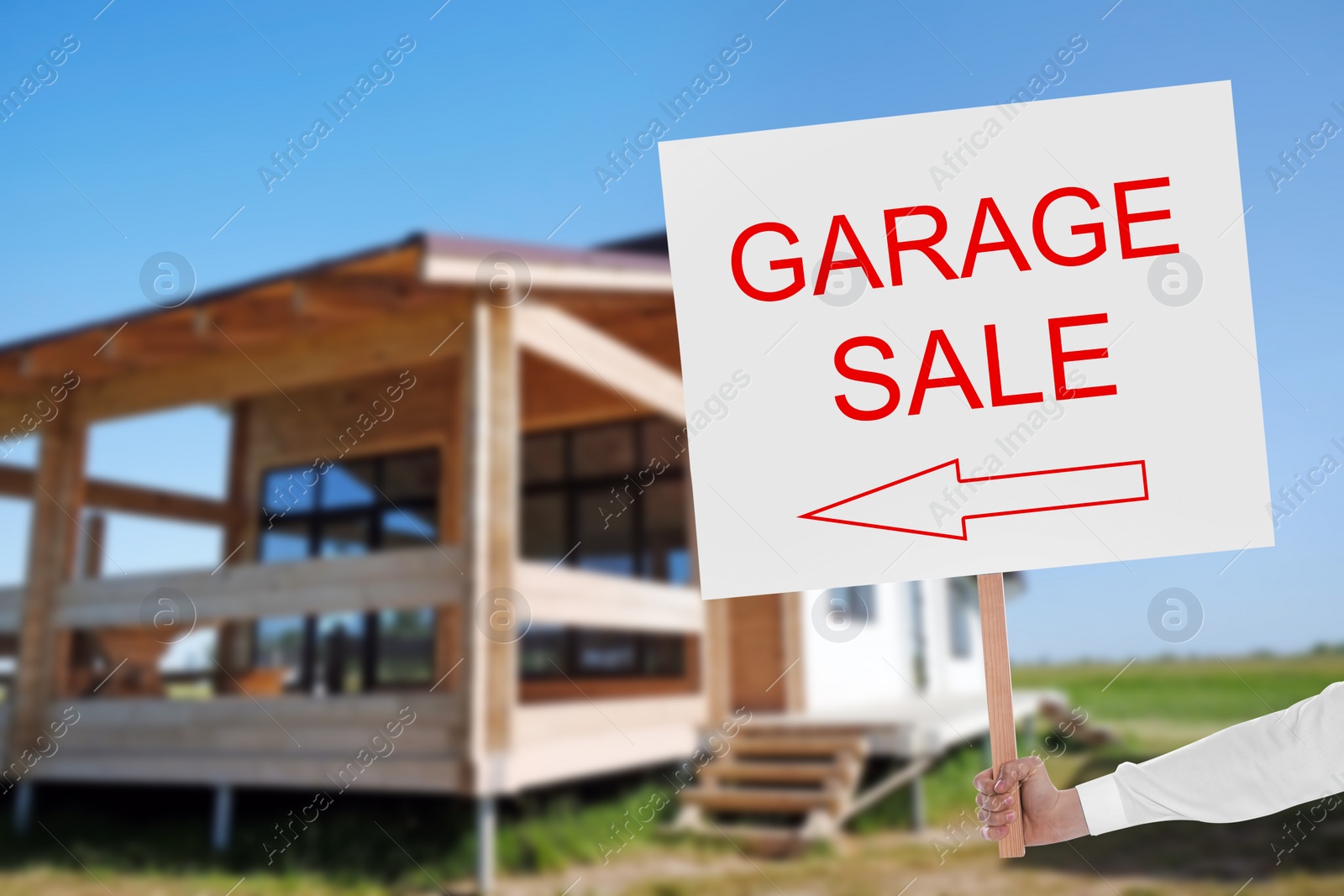 Image of Man holding sign with text GARAGE SALE near house on sunny day, closeup