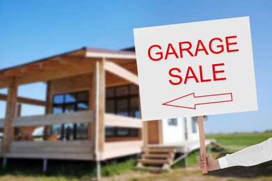 Image of Man holding sign with text GARAGE SALE near house on sunny day, closeup