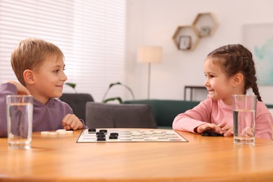 Photo of Cute children playing checkers at wooden table in room