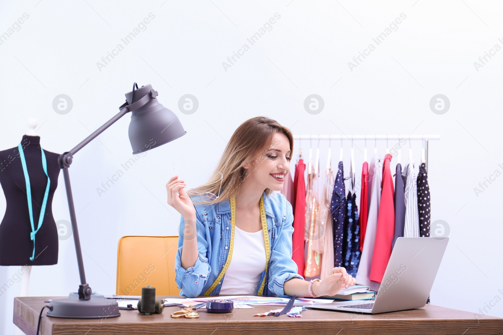 Photo of Beautiful young stylist at workplace near rack with clothes