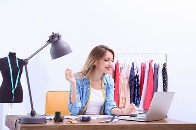 Beautiful young stylist at workplace near rack with clothes