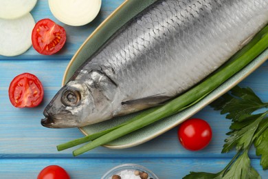 Photo of Delicious salted herring and fresh ingredients on light blue wooden table, flat lay