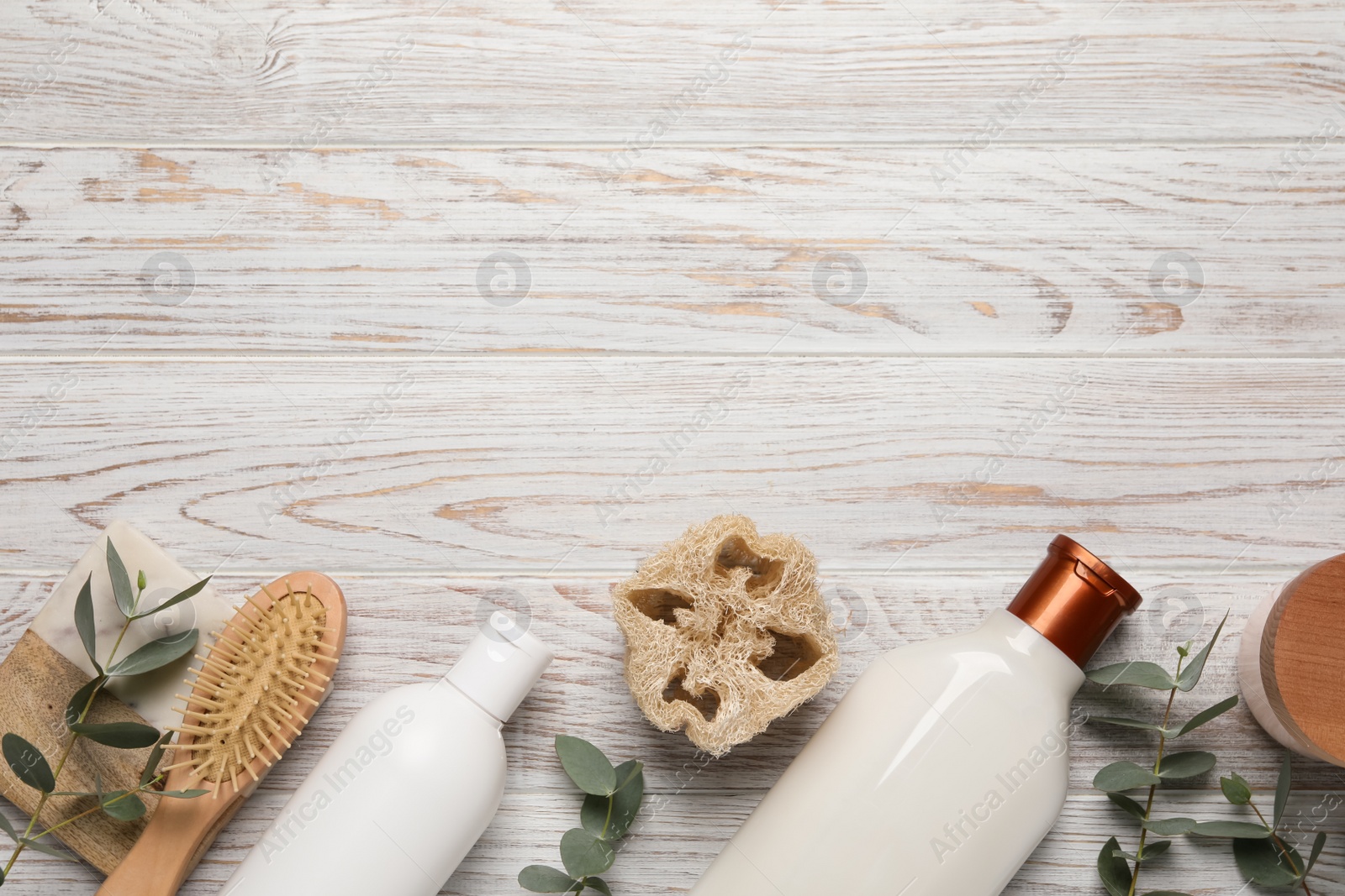 Photo of Shampoo bottles, loofah, hair brush and leaves on white wooden table, flat lay. Space for text