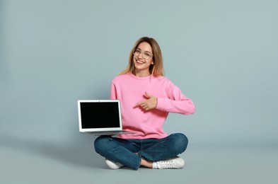 Young woman with modern laptop on grey background