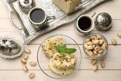 Photo of Tasty halva with pistachios and mint served on wooden table, flat lay