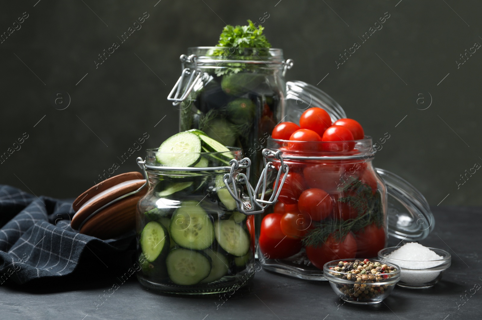 Photo of Pickling jars with fresh ripe vegetables and spices on black table