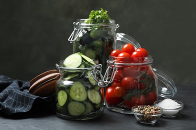 Pickling jars with fresh ripe vegetables and spices on black table