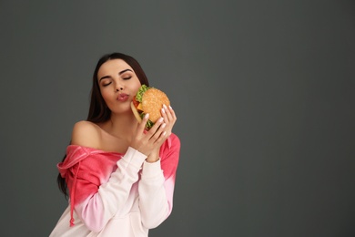 Photo of Young woman eating tasty burger on grey background. Space for text