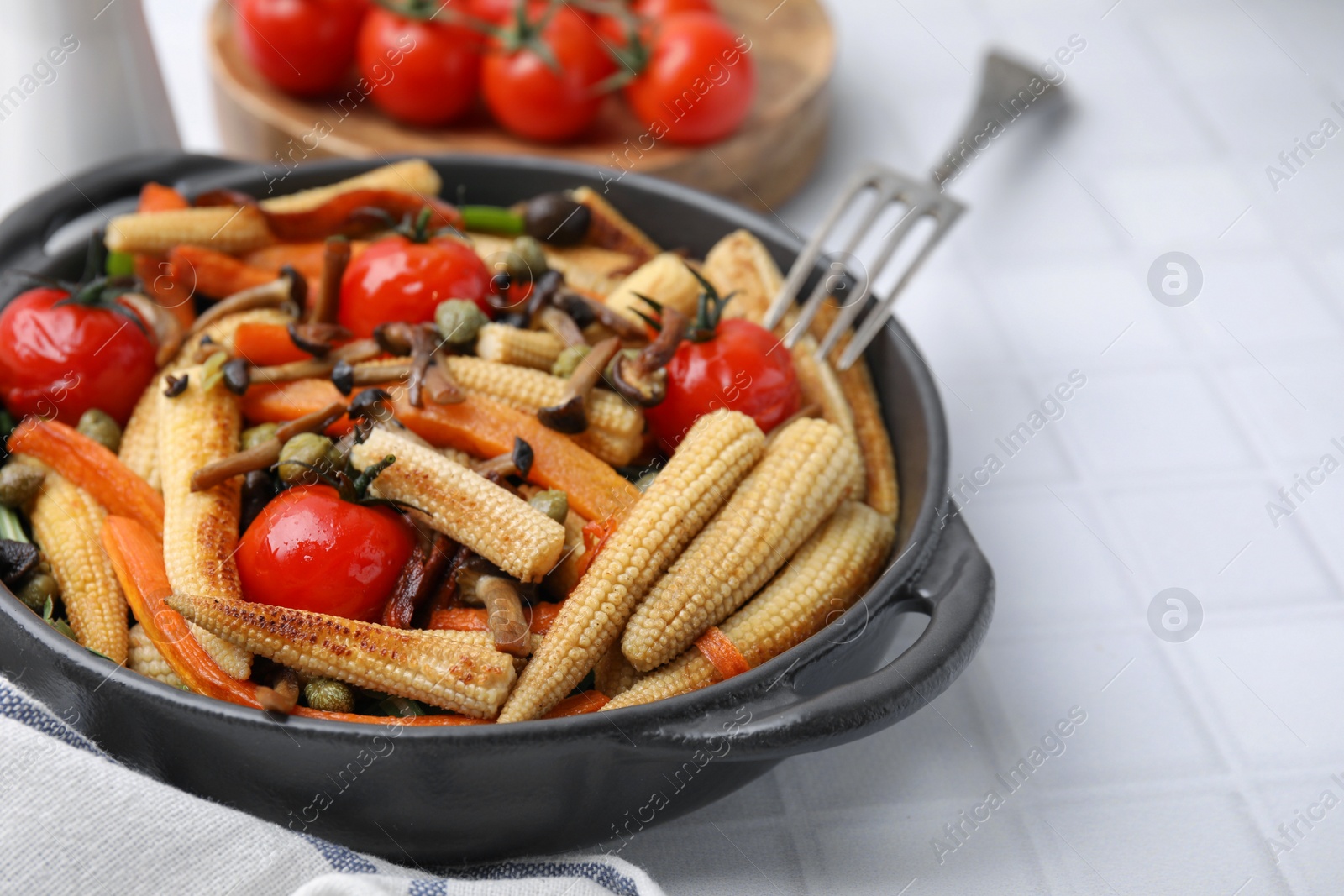 Photo of Tasty roasted baby corn with tomatoes, capers and mushrooms on white tiled table, closeup