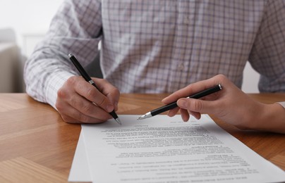 Photo of Businesspeople signing contract at wooden table, closeup of hands