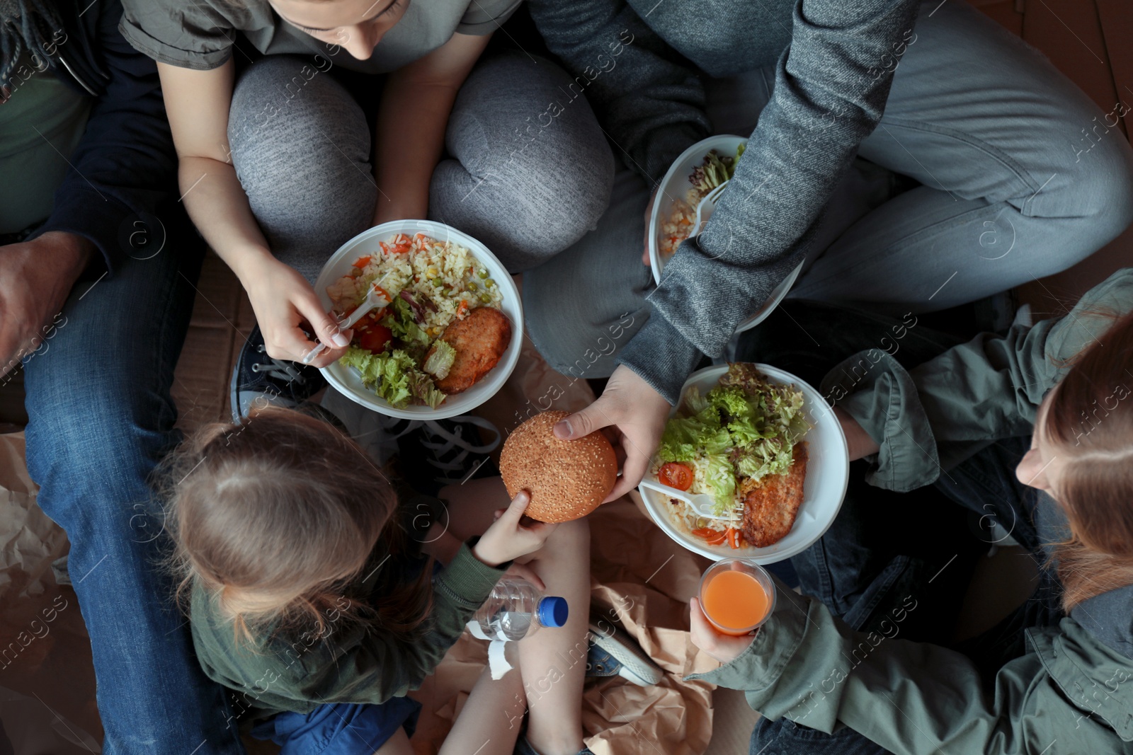 Photo of Poor people with plates of food sitting on floor indoors, view from above