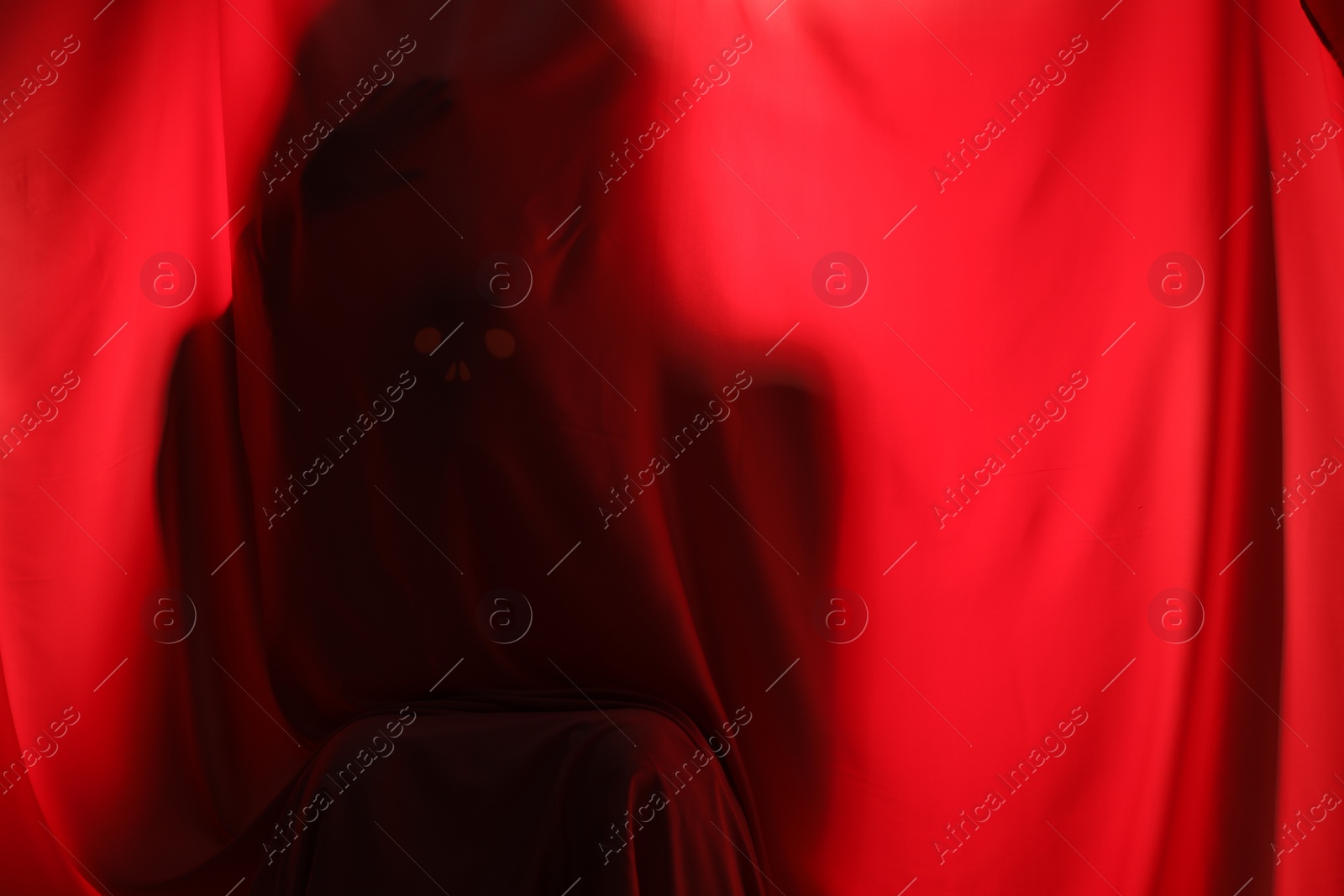 Photo of Silhouette of creepy ghost behind red cloth, space for text
