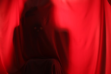 Silhouette of creepy ghost behind red cloth, space for text