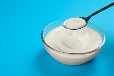 Eating tasty organic yogurt from bowl on light blue background, space for text